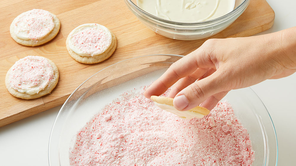 dipping frosted cookies in candy cane dust