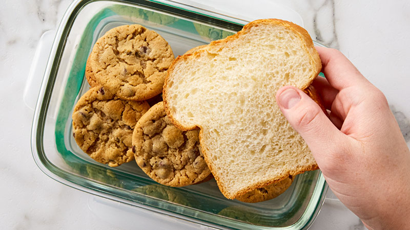 Chocolate chip cookies in a glass container with a slice of bread