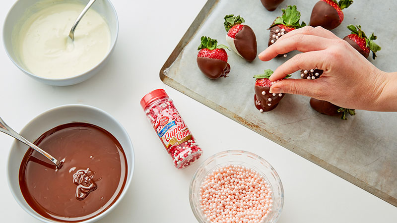 Bowls of white and dark chocolate; sprinkles, chocolate dipped strawberries on a baking sheet