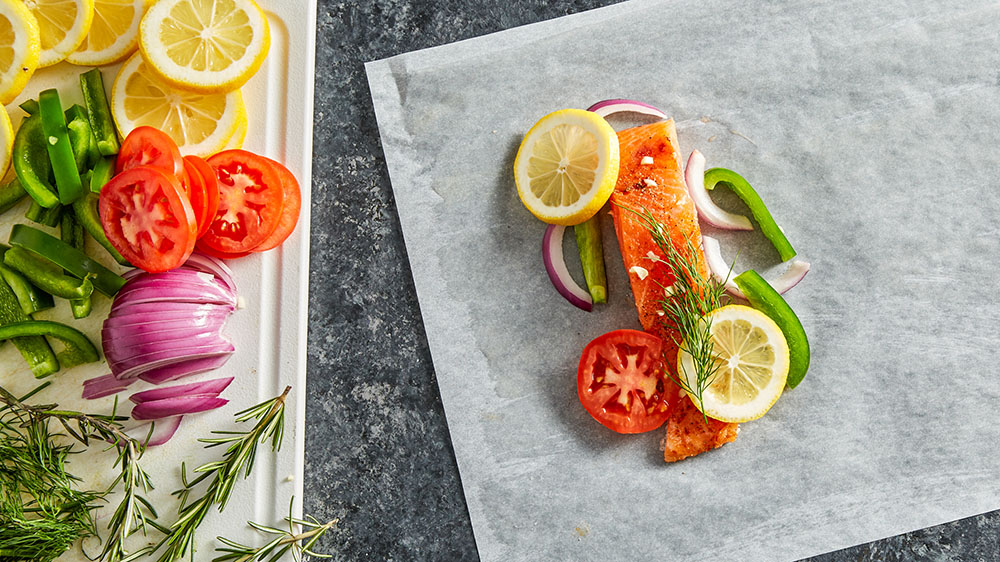 adding salmon, tomatoes, lemon, and peppers on top of parchment paper