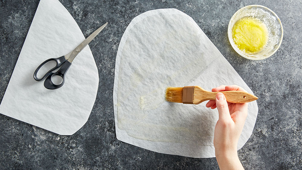 brushing butter on parchment onto rough heart shape