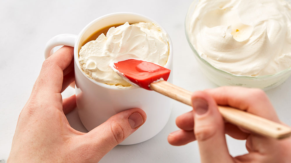 spreading whipped cream with spatula on top of latte