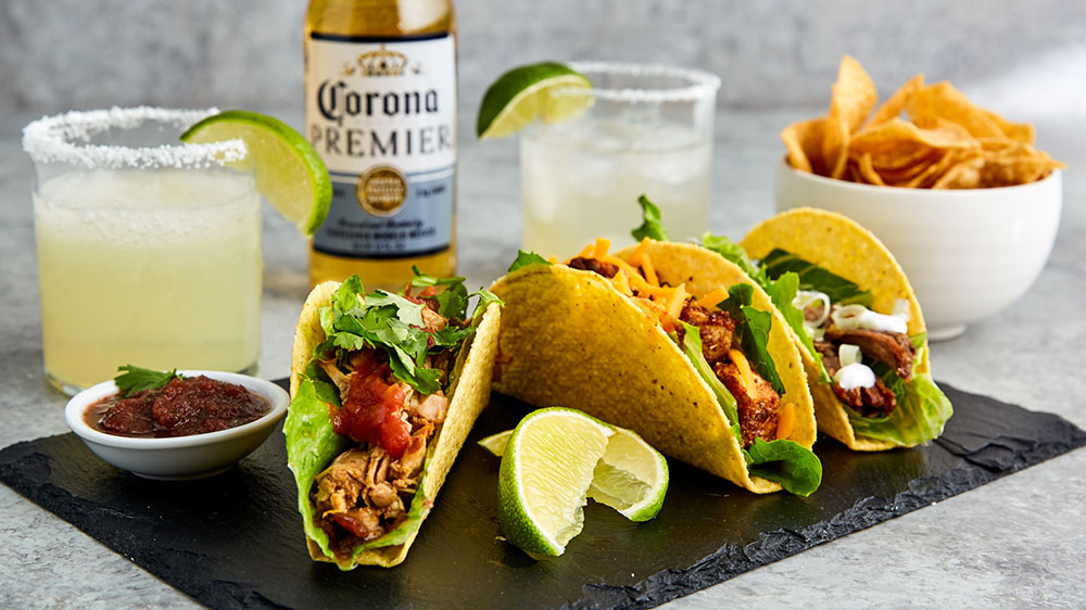 three tacos on a plate with chils and a corona beer